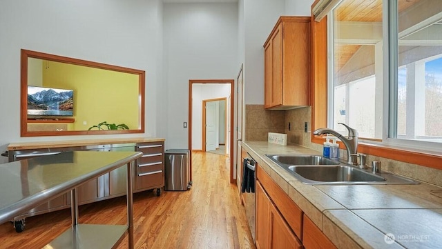 kitchen featuring a sink, decorative backsplash, brown cabinets, light wood-style floors, and stainless steel dishwasher