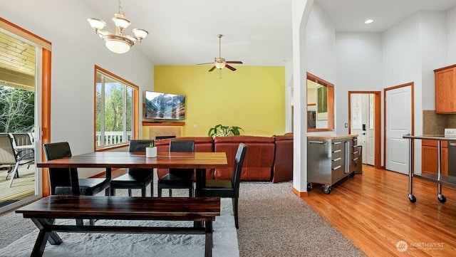 dining room featuring recessed lighting, a fireplace, a towering ceiling, ceiling fan with notable chandelier, and light wood-type flooring