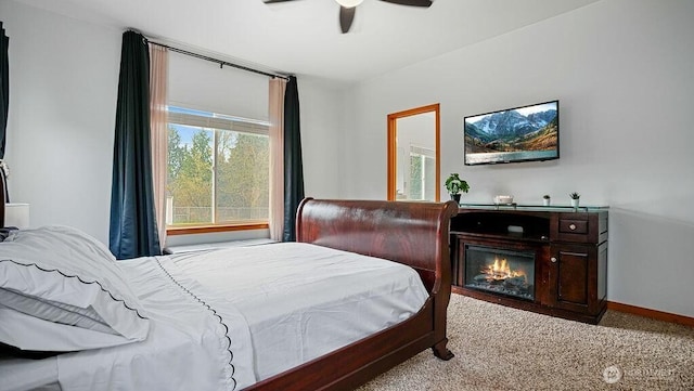 bedroom with a glass covered fireplace, a ceiling fan, baseboards, and carpet floors