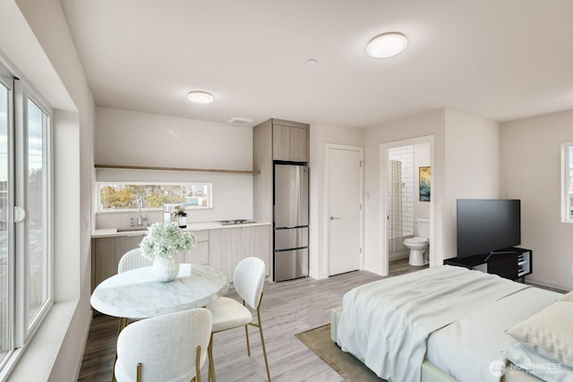 bedroom featuring ensuite bathroom, light wood finished floors, a sink, and freestanding refrigerator