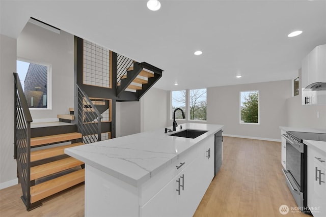 kitchen featuring light wood finished floors, dishwasher, electric range oven, white cabinetry, and a sink