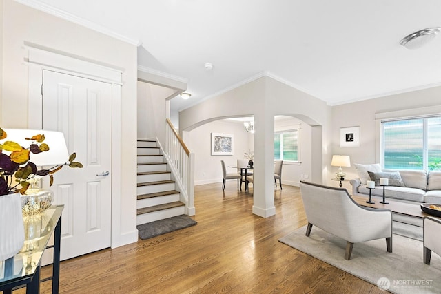 living area with stairway, crown molding, arched walkways, and wood finished floors