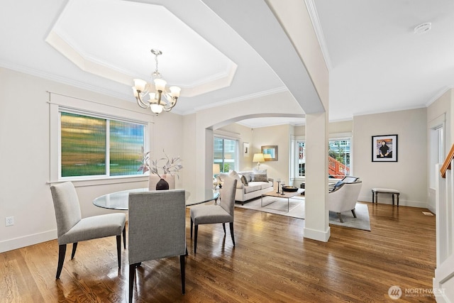 dining room featuring arched walkways, ornamental molding, wood finished floors, a chandelier, and baseboards