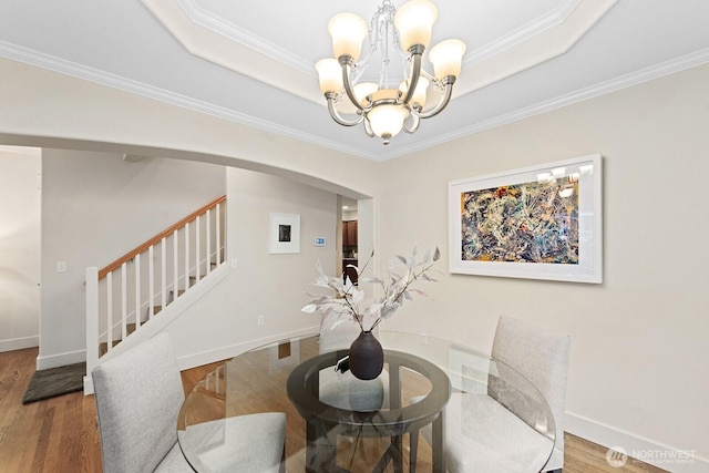 dining space with stairs, a tray ceiling, arched walkways, and wood finished floors