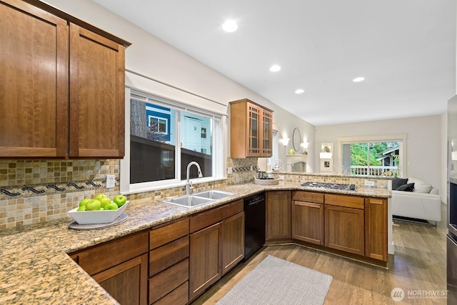 kitchen with black dishwasher, light wood-style floors, open floor plan, a sink, and a peninsula