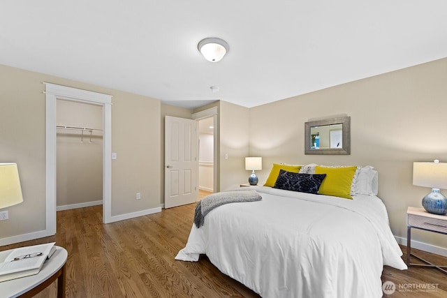 bedroom featuring a walk in closet, a closet, baseboards, and wood finished floors