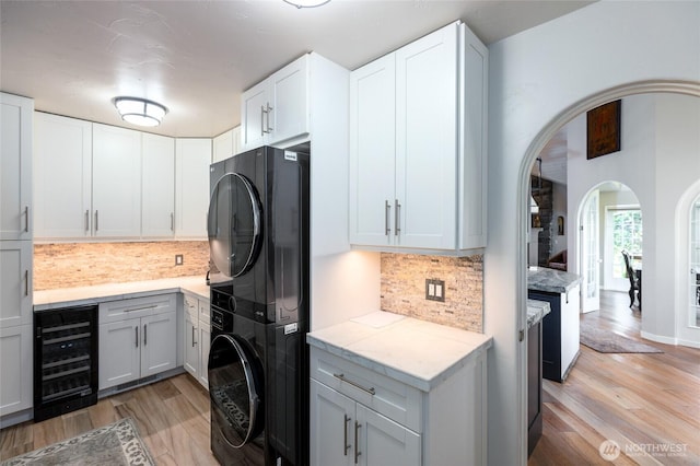 kitchen featuring arched walkways, wine cooler, light wood-style flooring, tasteful backsplash, and stacked washer and clothes dryer