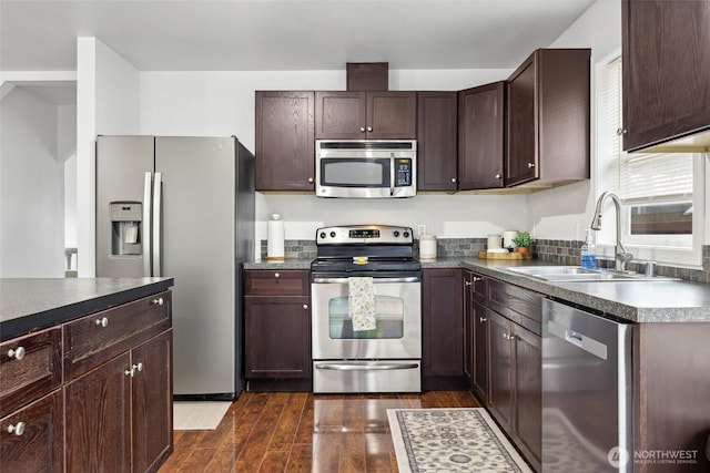 kitchen with appliances with stainless steel finishes, dark wood-style flooring, a sink, and dark brown cabinets