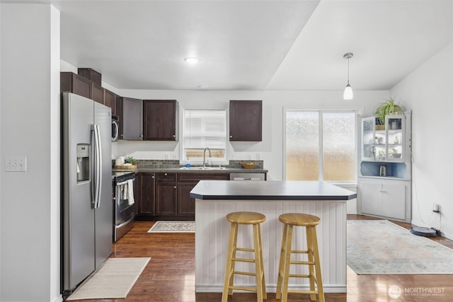 kitchen featuring dark brown cabinetry, dark wood-style floors, a kitchen island, appliances with stainless steel finishes, and a breakfast bar