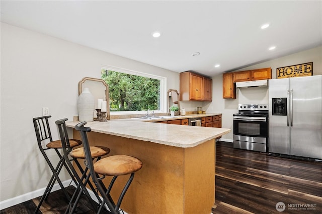 kitchen with brown cabinets, light countertops, appliances with stainless steel finishes, a peninsula, and under cabinet range hood