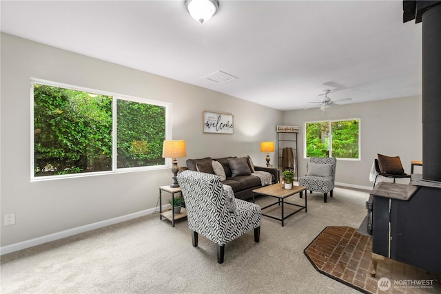 carpeted living room featuring a wood stove, ceiling fan, and baseboards