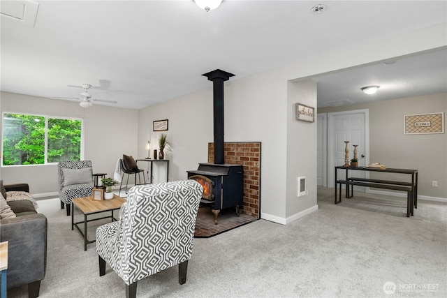 living area with baseboards, visible vents, a ceiling fan, a wood stove, and carpet