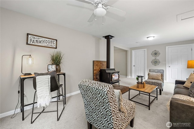 living area with light carpet, a wood stove, baseboards, and a ceiling fan