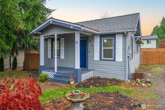 bungalow featuring covered porch, a shingled roof, and fence