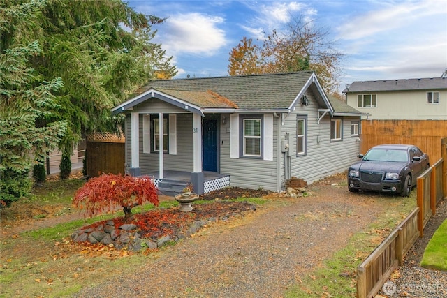 bungalow-style house featuring driveway, a porch, a shingled roof, and fence