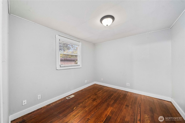 spare room featuring dark wood finished floors, visible vents, and baseboards