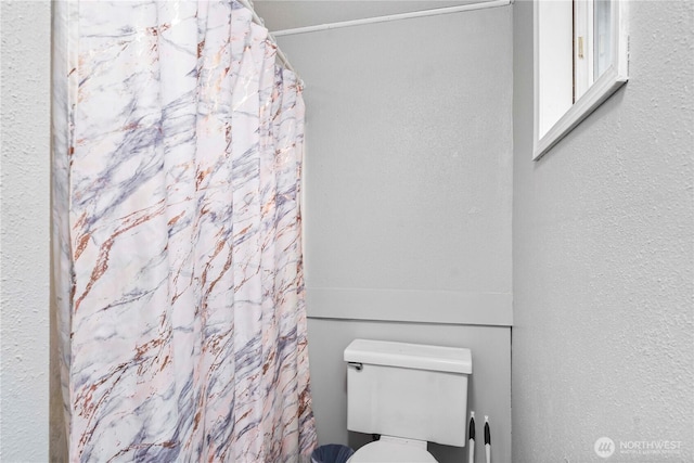 bathroom with toilet, a shower with curtain, and a textured wall