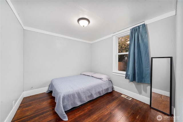 bedroom with hardwood / wood-style flooring, baseboards, visible vents, and crown molding