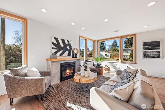 living area featuring a tiled fireplace, visible vents, wood finished floors, and recessed lighting