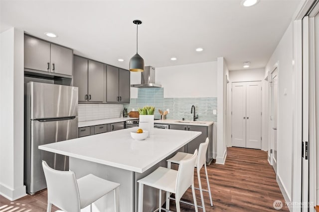 kitchen featuring stainless steel appliances, gray cabinets, a sink, and wall chimney exhaust hood