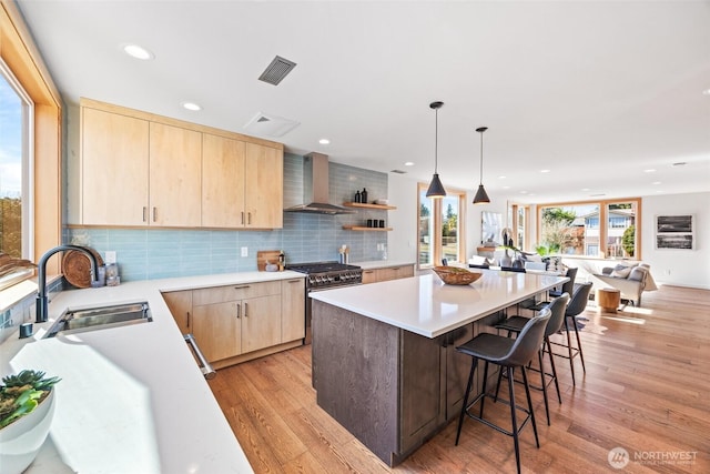 kitchen featuring light brown cabinets, a sink, visible vents, wall chimney range hood, and high end stainless steel range