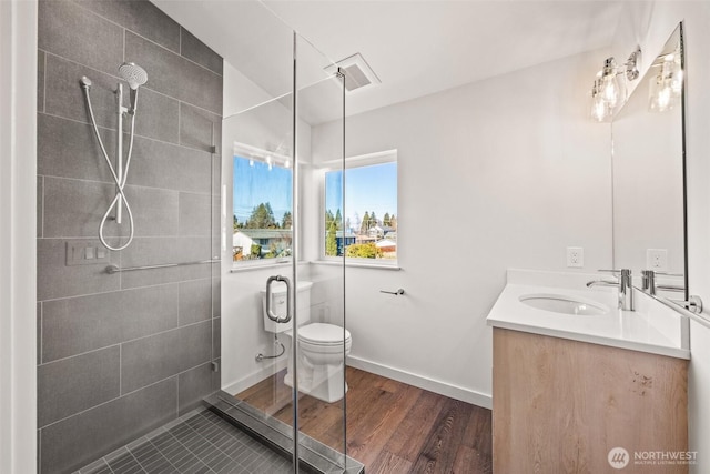 bathroom with a stall shower, baseboards, toilet, wood finished floors, and vanity