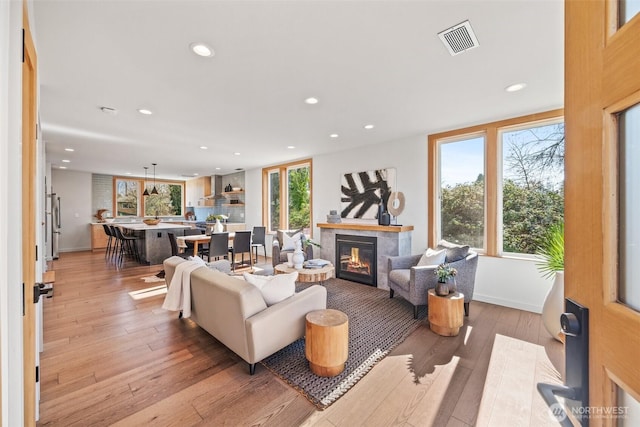 living room featuring light wood finished floors, a glass covered fireplace, visible vents, and recessed lighting