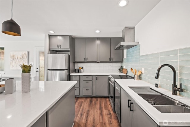 kitchen featuring gray cabinetry, a sink, appliances with stainless steel finishes, dark wood-style floors, and wall chimney exhaust hood