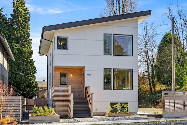 modern home with stairs, fence, and stucco siding