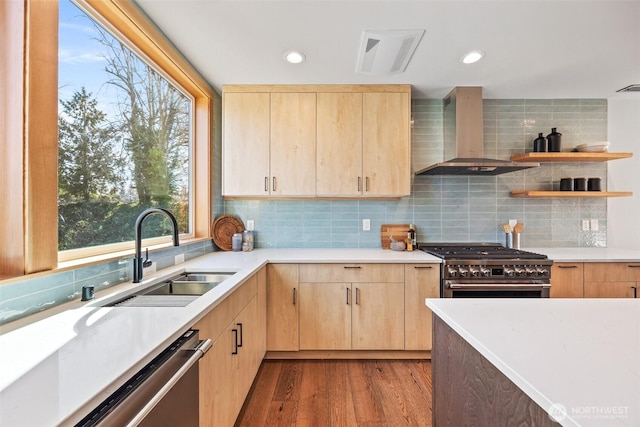 kitchen with stainless steel appliances, a sink, visible vents, wall chimney range hood, and light brown cabinetry