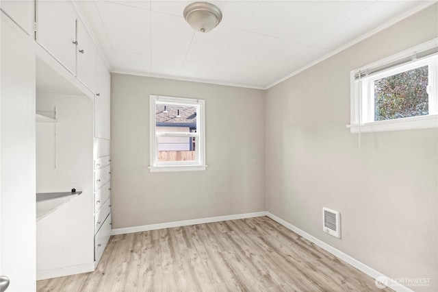 empty room featuring light wood-style floors, baseboards, visible vents, and crown molding