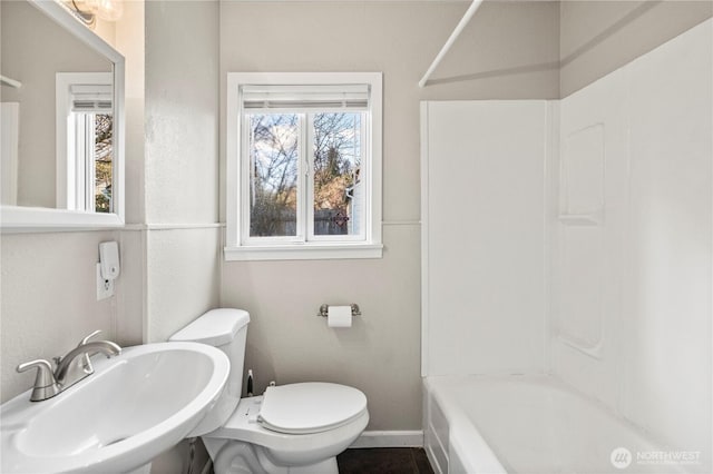 full bath featuring toilet, baseboards,  shower combination, and a sink