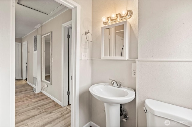 half bathroom featuring crown molding, a textured wall, toilet, wood finished floors, and baseboards