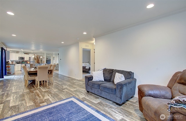 living room featuring light wood finished floors, ornamental molding, and recessed lighting