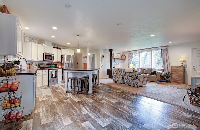 kitchen featuring dark countertops, appliances with stainless steel finishes, open floor plan, a sink, and light wood-type flooring