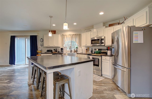 kitchen with dark countertops, appliances with stainless steel finishes, white cabinetry, a sink, and wood finished floors