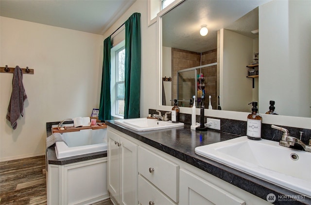 full bathroom featuring double vanity, wood finished floors, a stall shower, and a sink