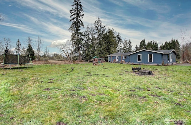 view of yard with a trampoline, a playground, and a fire pit