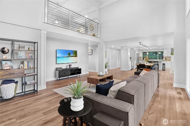 living area with baseboards, light wood-style flooring, and a high ceiling