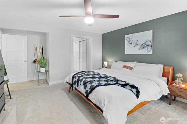 bedroom with a closet, light colored carpet, ceiling fan, and baseboards