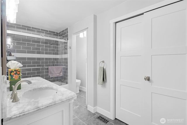 full bathroom with toilet, a sink, baseboards, tiled shower, and double vanity