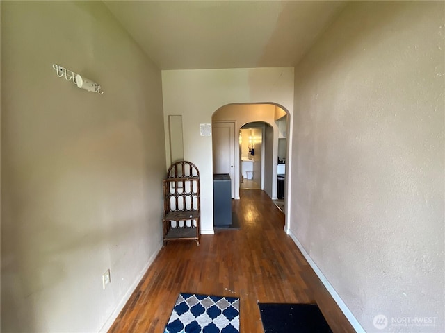 hallway with arched walkways, wood finished floors, and baseboards