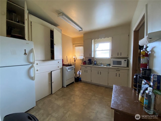 kitchen featuring white appliances, white cabinetry, light floors, and a sink