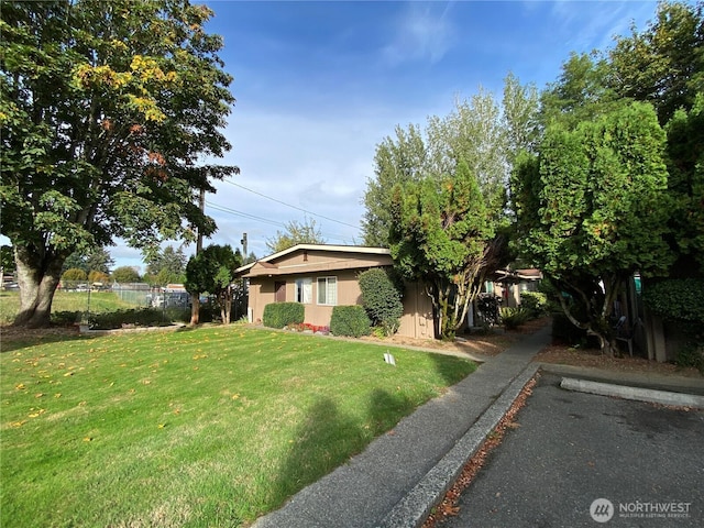 view of front of home with uncovered parking, fence, a front lawn, and stucco siding