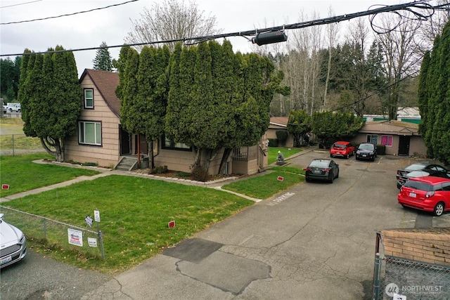 view of front of property with uncovered parking, a front yard, fence, and a shingled roof