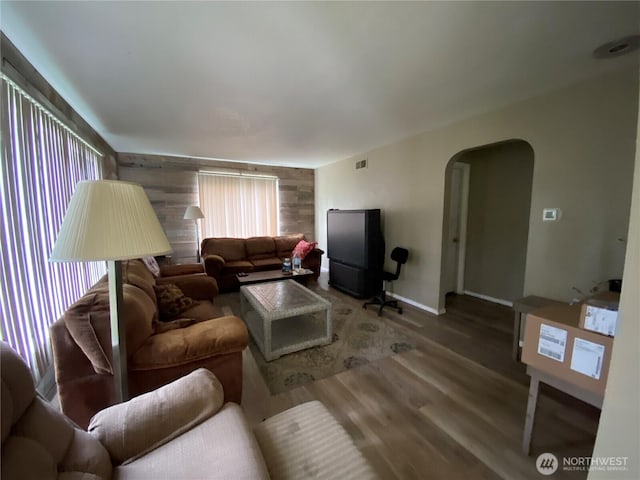 living room featuring arched walkways, wood finished floors, visible vents, and baseboards