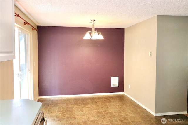 unfurnished dining area featuring baseboards, a textured ceiling, and an inviting chandelier