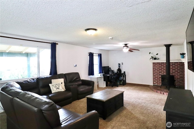 carpeted living area with a wood stove, a healthy amount of sunlight, ceiling fan, and a textured ceiling