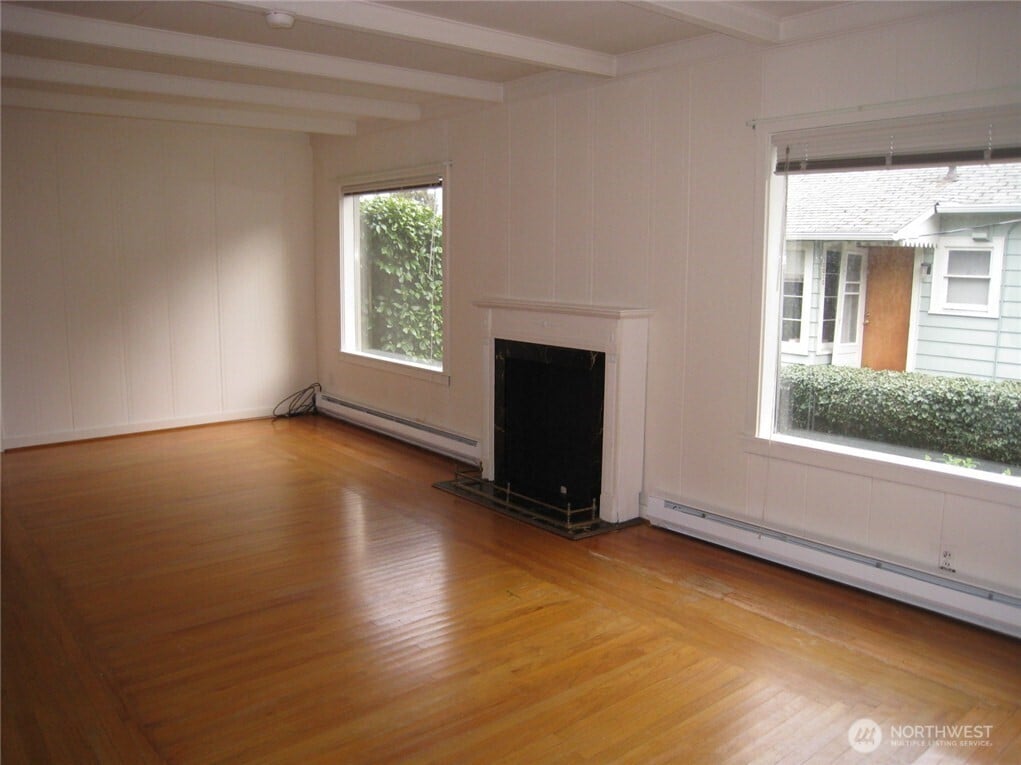 unfurnished living room featuring beam ceiling, a fireplace, a baseboard radiator, a baseboard heating unit, and wood finished floors