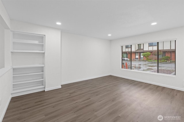 empty room with built in shelves, recessed lighting, baseboards, and wood finished floors